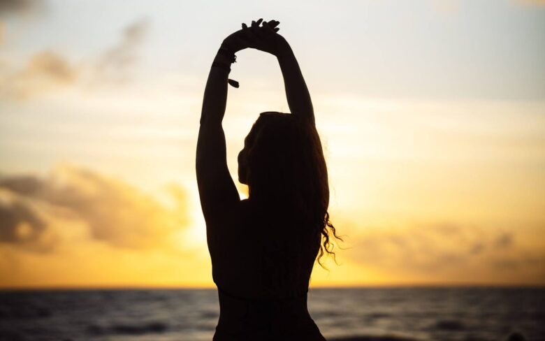 Silueta de mujer estirándose al atardecer junto al mar, vivir en renovación