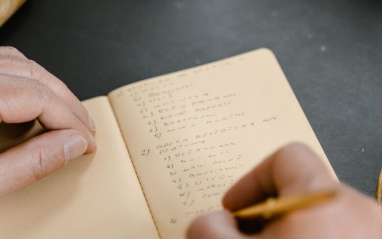 Vista desde arriba de unas manos sobre una libreta abierta, escribiendo una lista a mano