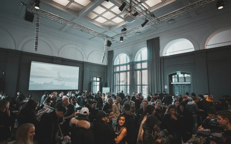 Salón amplio con ventanales en arco, lleno de gente de pie conversando durante un evento